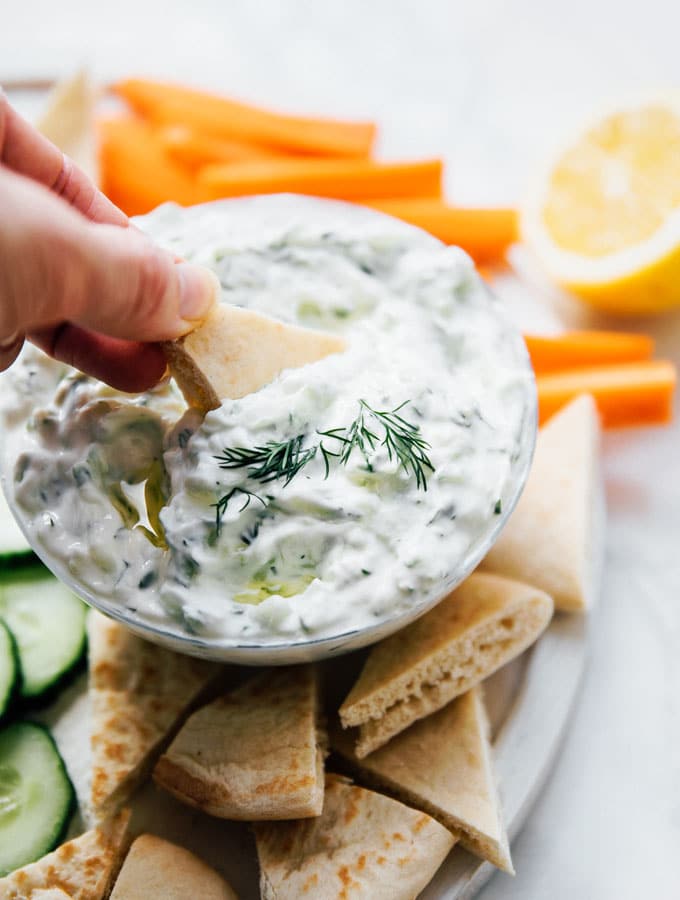 Best tzatziki recipe with pita bread and veggies on a marble table.