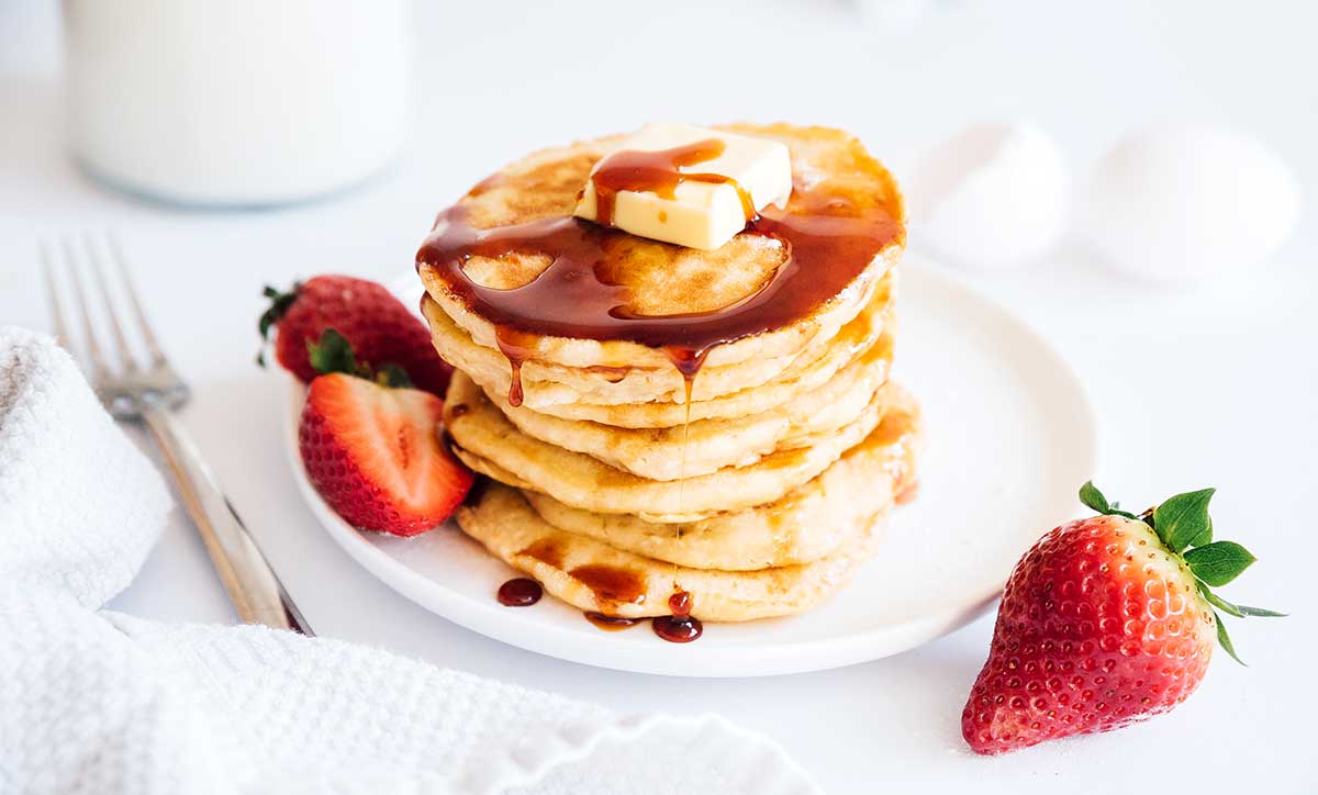 Pancakes stacked on a plate with strawberry and butter with syrup dripping