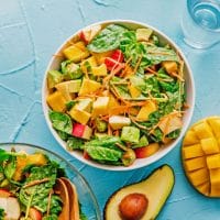 Salad with spinach, mango, carrots, and apple in a bowl on a blue background