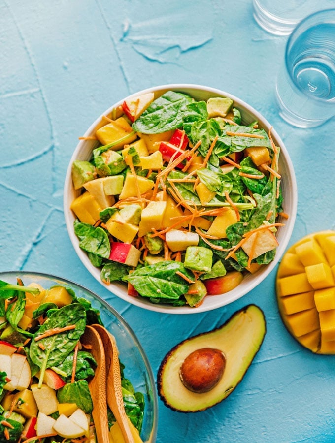 Salad with spinach, mango, carrots, and apple in a bowl on a blue background