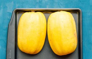 Two halved spaghetti squash placed cut side down on a baking tray, ready to be transformed into a delicious dish featuring savory mushrooms, over a blue surface.