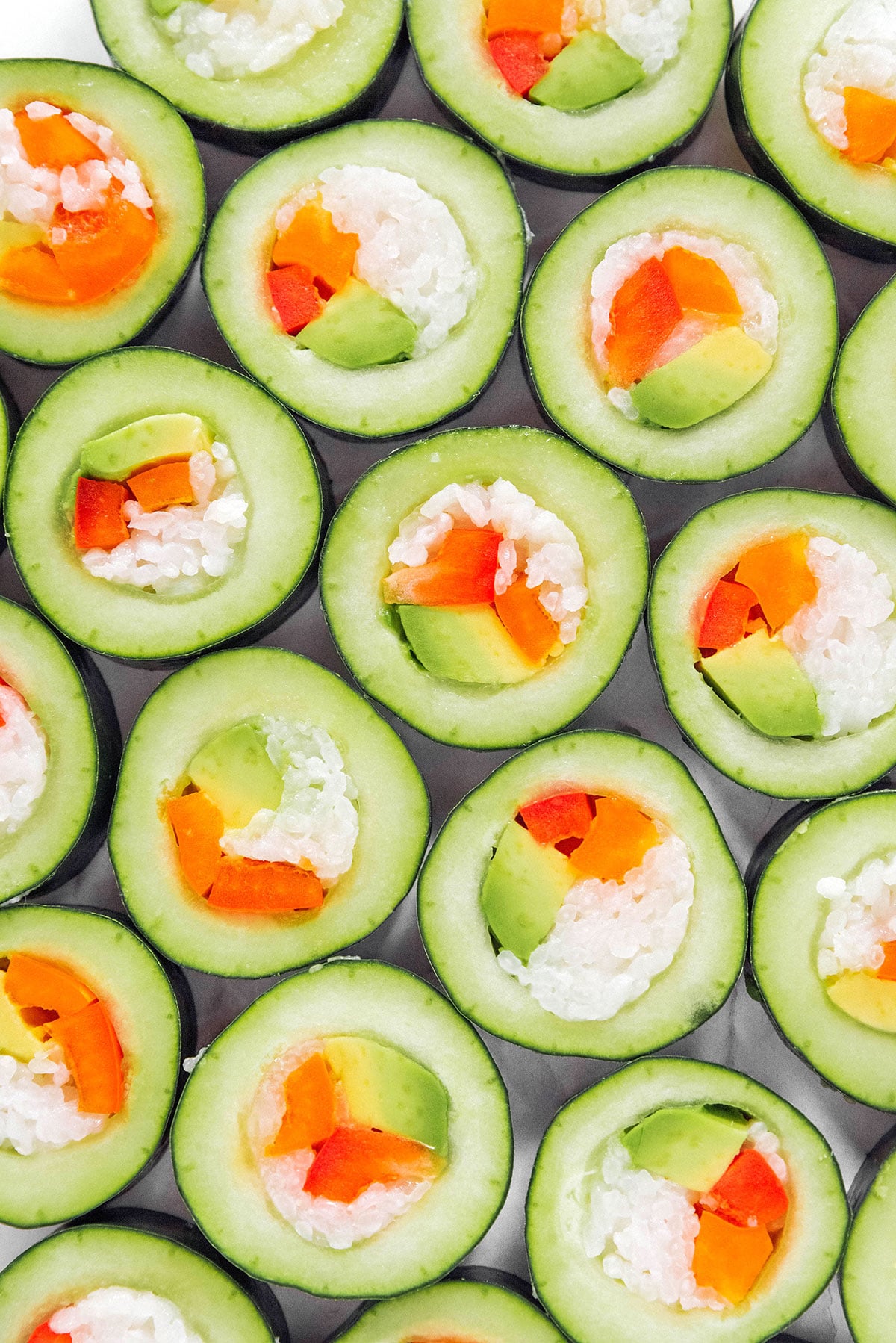 Closeup of stuffed cucumber sushi with rice, carrots, and avocado