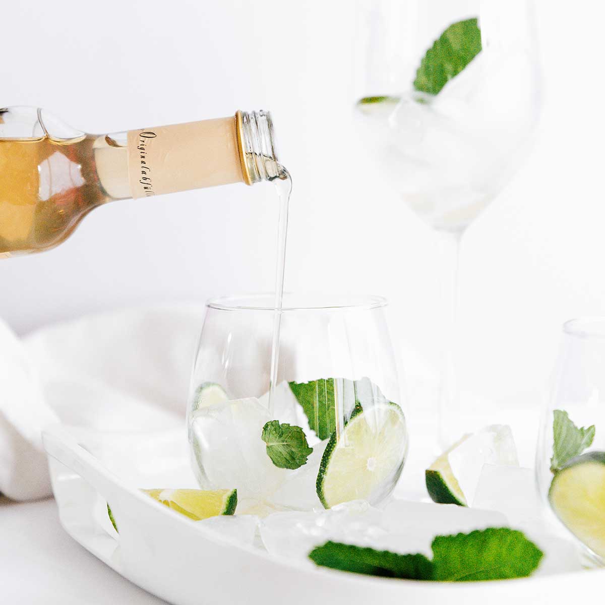 Pouring elderflower syrup into a hugo spritz cocktail in a glass with lime and mint