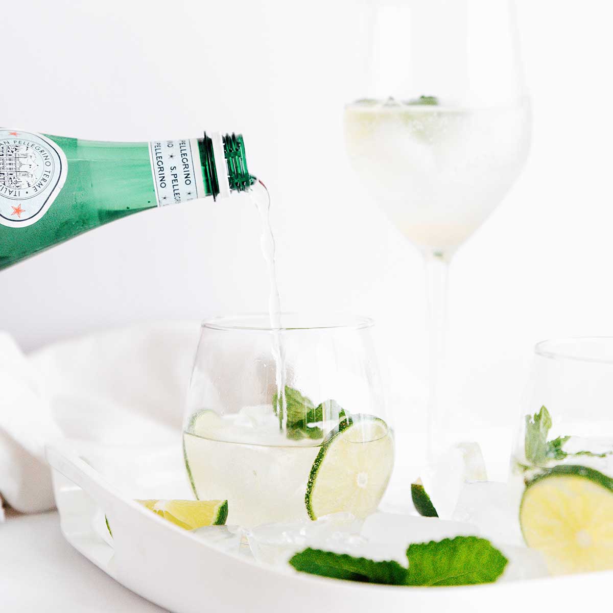 Pouring sparkling water into a hugo spritz cocktail in a glass with lime and mint