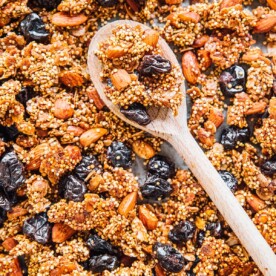 Close-up of a wooden spoon resting on quinoa granola, filled with almonds, puffed quinoa, and dried berries.