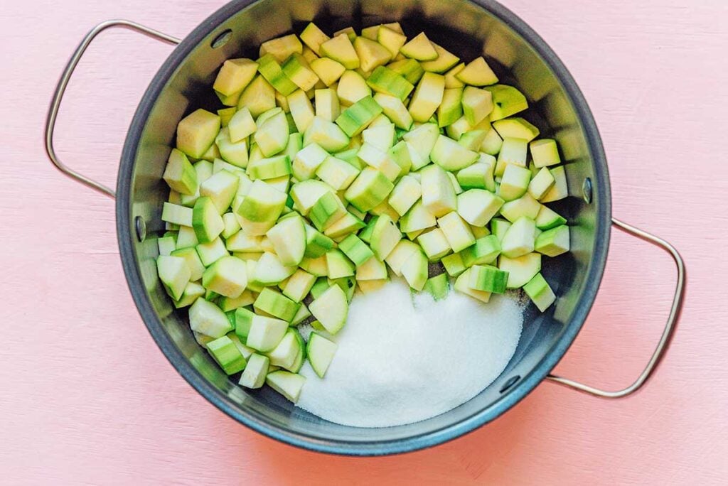 A cooking pot filled with peeled and chopped zucchini and sugar