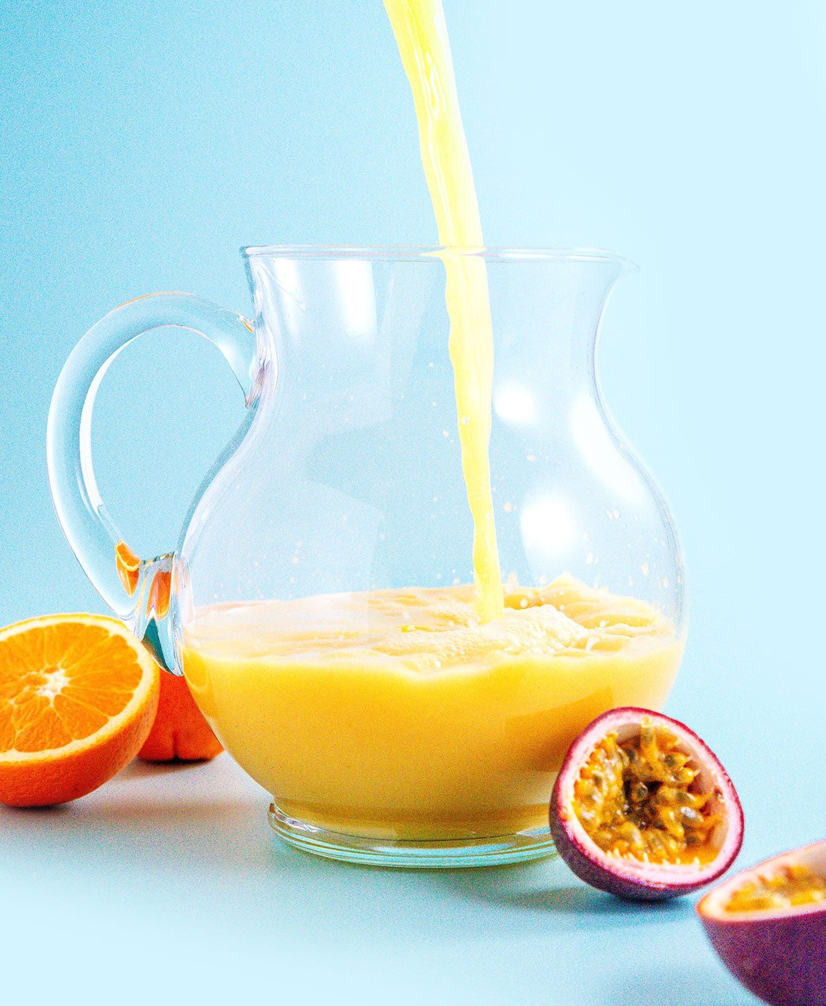 Pouring orange juice into a pitcher with a blue background
