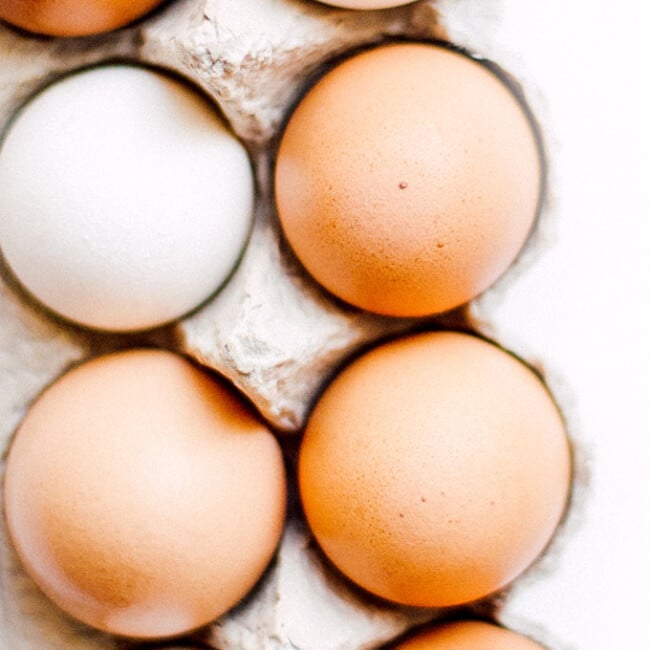 White and brown eggs in a carton on a white background
