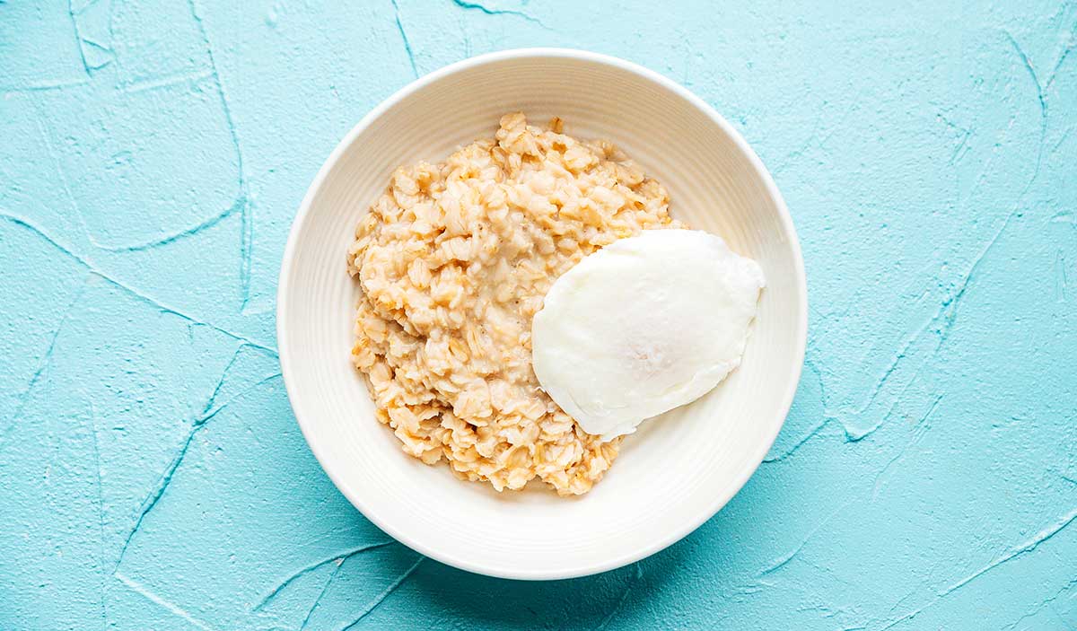 Oatmeal with an egg in a white bowl on a blue background