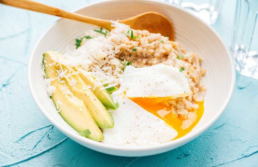Oatmeal with egg and avocado in a white bowl on a blue background