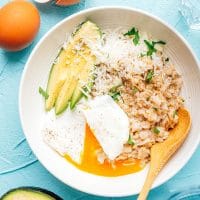 Savory oatmeal with egg and avocado in a white bowl on a blue background