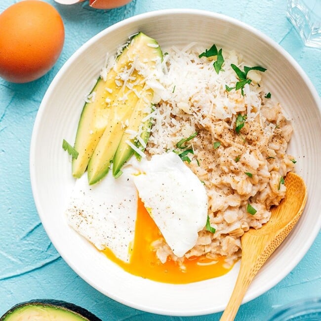 Savory oatmeal with egg and avocado in a white bowl on a blue background