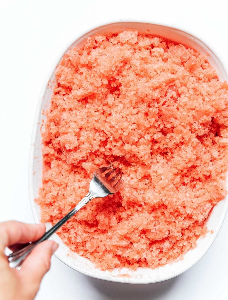 Scraping watermelon granita with a fork in a white dish