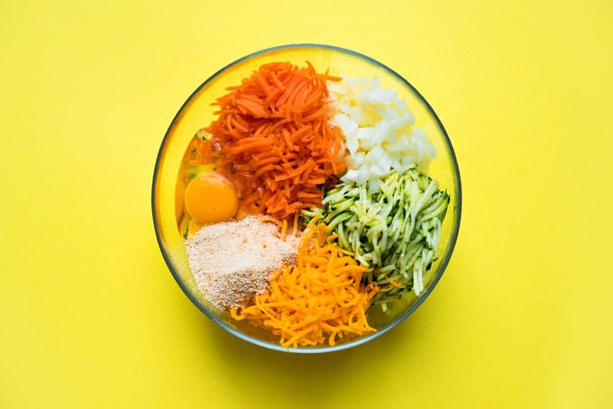A clear glass bowl filled with various zucchini cheddar bite ingredients
