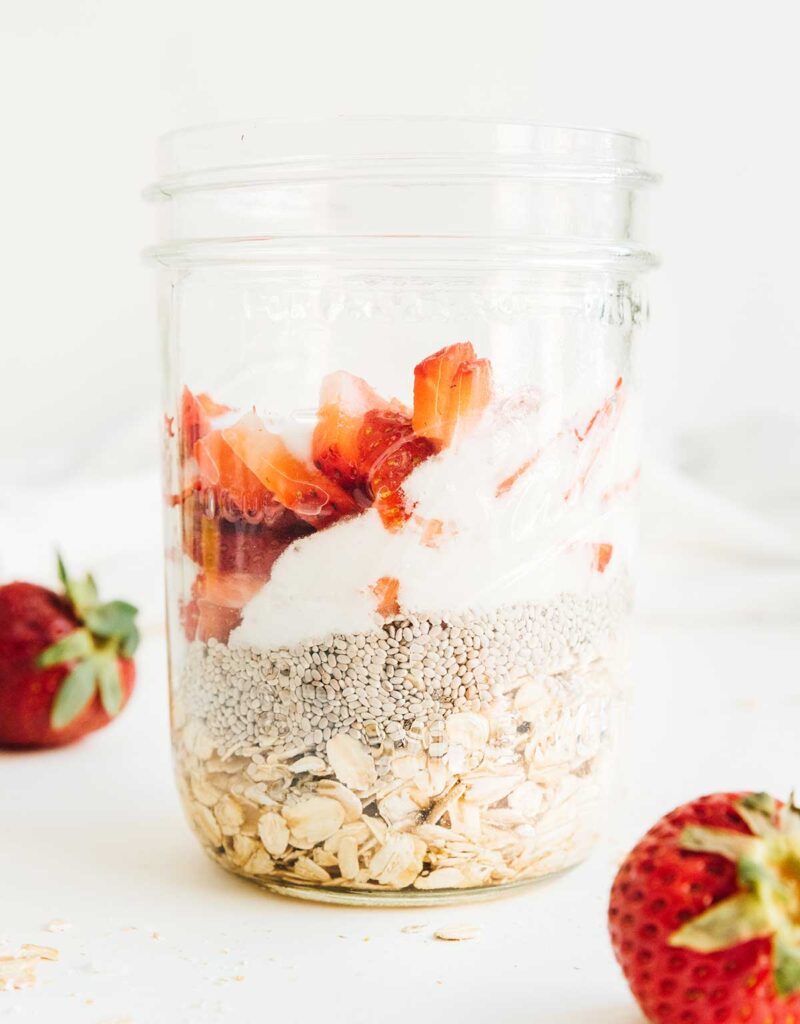 A mason jar filled with strawberries and cream overnight oats ingredients