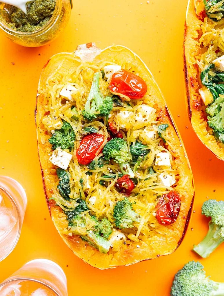 A completed pesto spaghetti squash bowl filled with squash noodles, spinach, broccoli, tomatoes, feta, and pesto