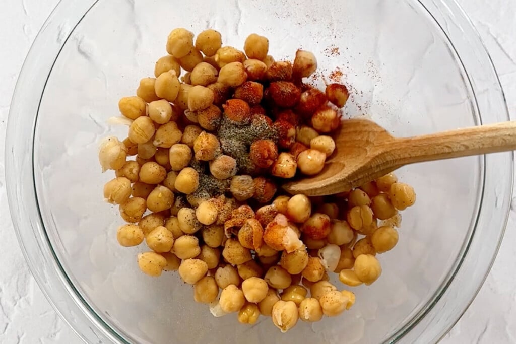 Stirring chickpeas and spices in glass bowl.