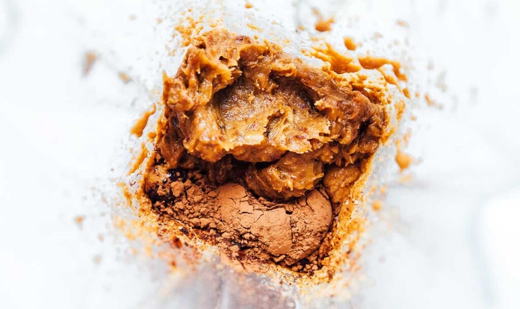 A food processor filled with pureed dates, hazelnut nut butter, and cocoa powder