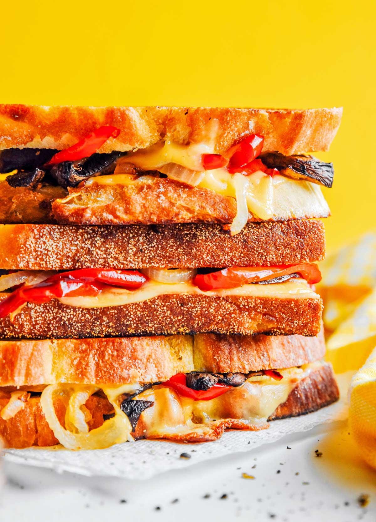 Close up view of 3 stacked roasted vegetable grilled cheeses displaying the fillings of pepper, onion, mushrooms, and gouda