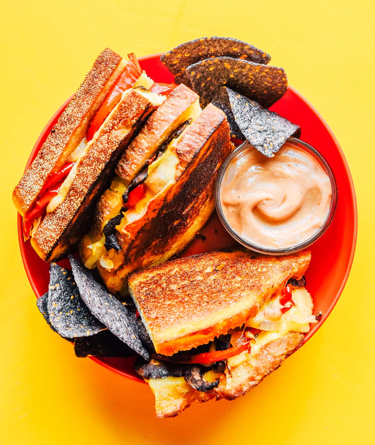 A plate filled with three roasted vegetable paninis, toasty sauce, and tortilla chips