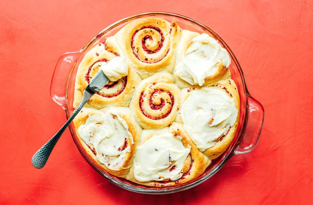 A glass baking dish filled with cranberry orange cinnamon rolls, four of which have been iced