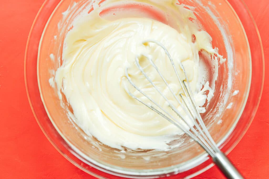 A clear glass bowl filled with icing ingredients being whisked