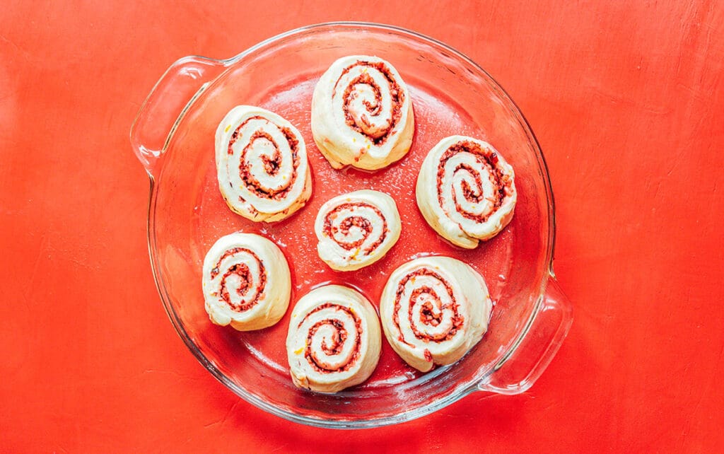 A glass baking dish filled with seven cranberry orange cinnamon rolls that have not yet risen