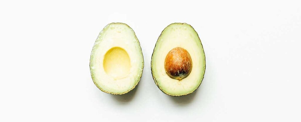 Two halves of an avocado placed inside-up and side by side on a white background