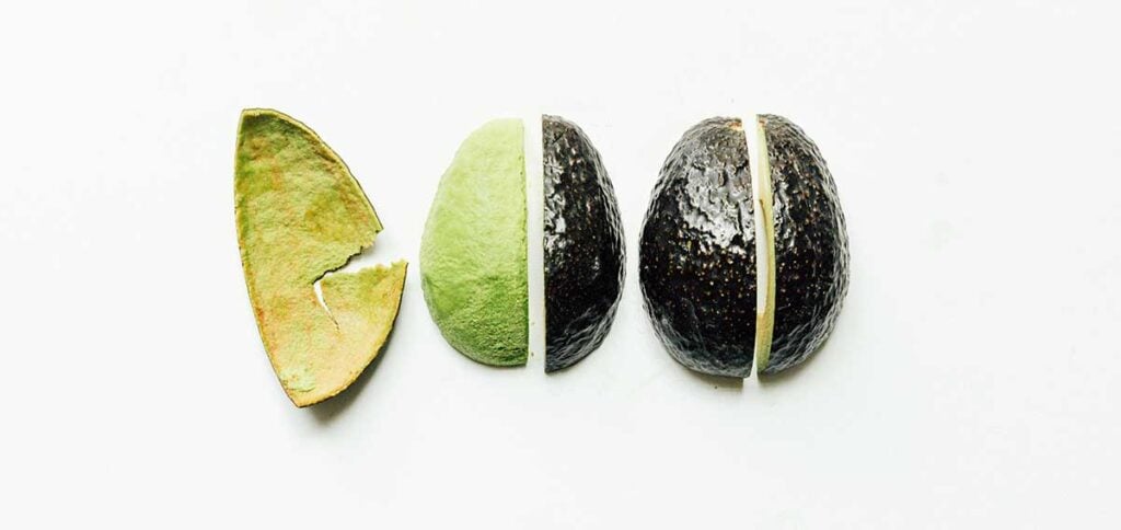 Four quarters of an avocado facing down displaying how to peel the skin from a quarter of the fruit