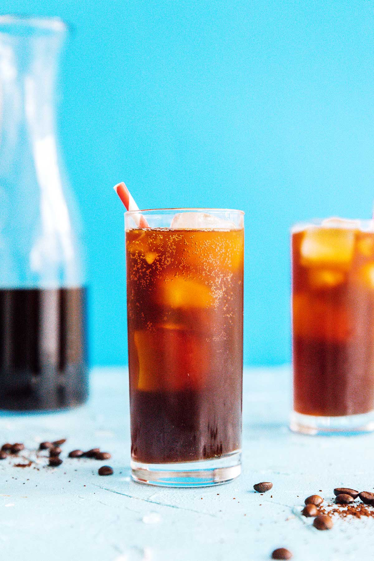 Fizzy coffee in a tall glass with a straw on a blue background