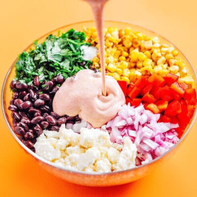 Pouring sauce into a bowl of elote salad