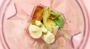 Inside a blender: sliced banana, creamy avocado pieces, and rich cocoa powder mix harmoniously, promising a luscious avocado smoothie experience from above.