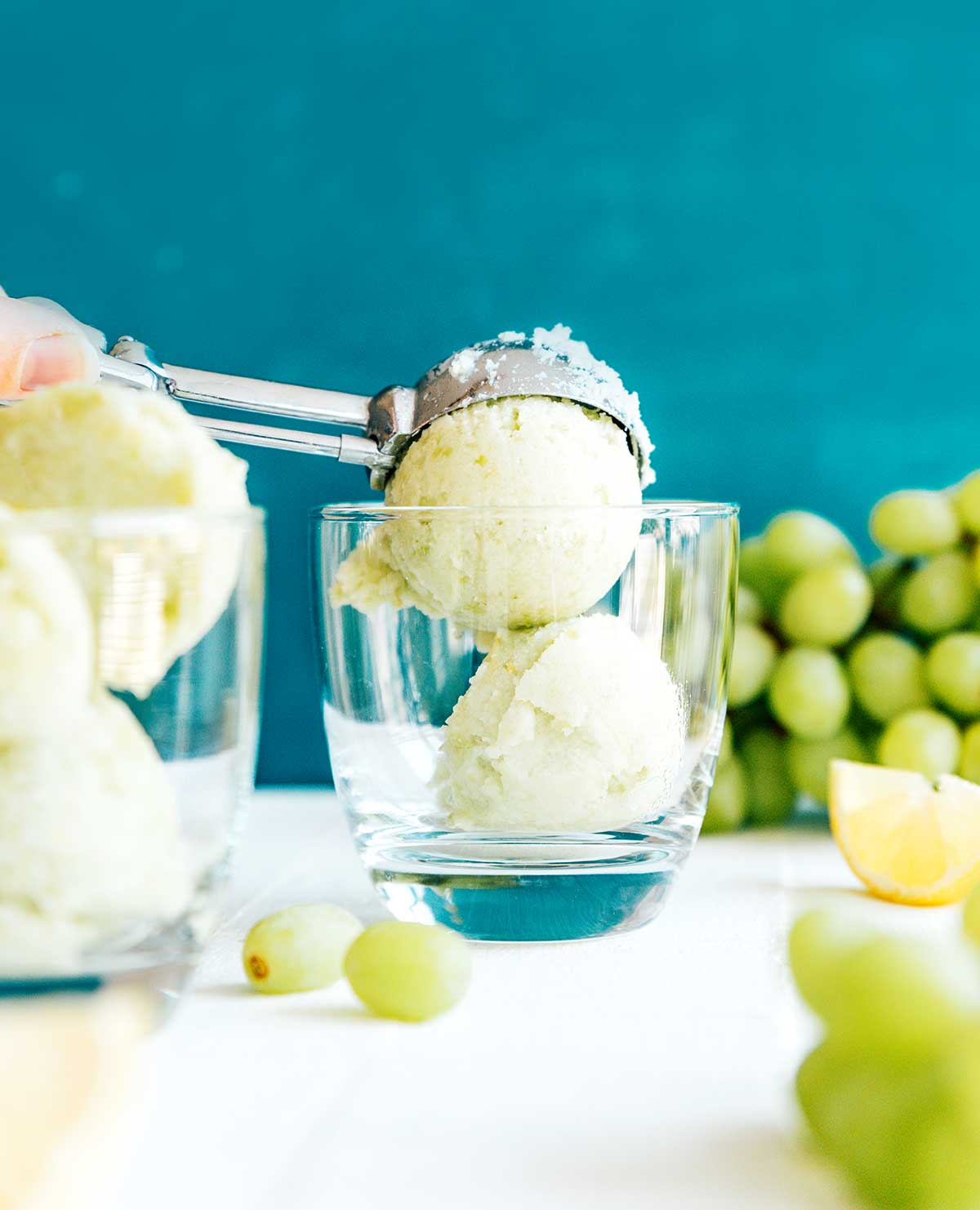 Scooping green grape sorbet into a glass on a blue background