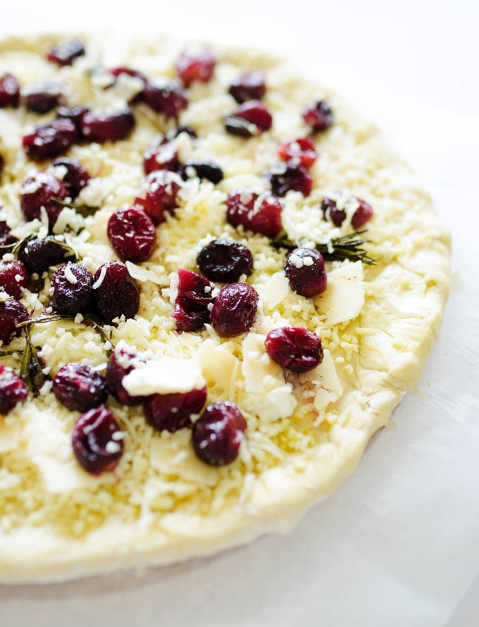 An uncooked 3 cheese roasted grape pizza topped with ricotta, parmesan, mozzarella, roasted grapes, and rosemary