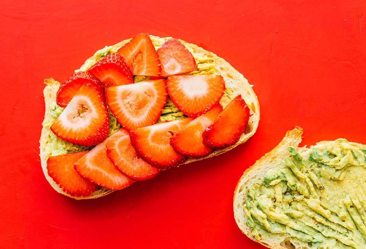 Two slices of avocado bread topped with avocado and one half topped with strawberries
