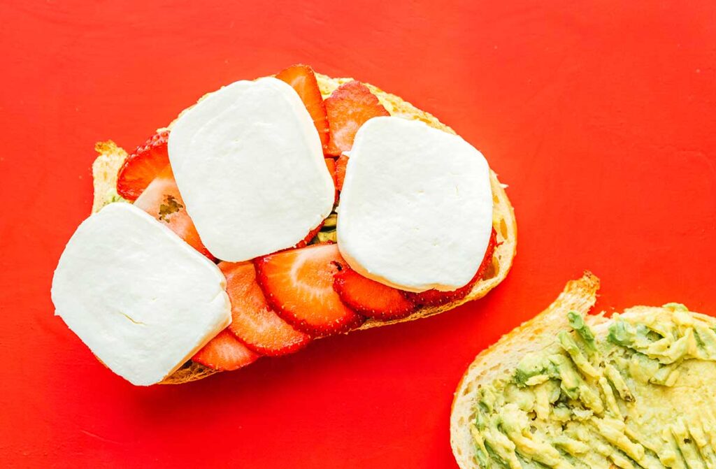 Two slices of avocado bread topped with avocado and one half topped with strawberries and mozzarella
