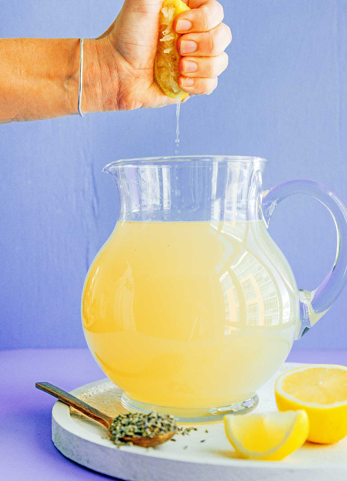 A hand squeezing lemon juice into a pitcher of lavender lemonade