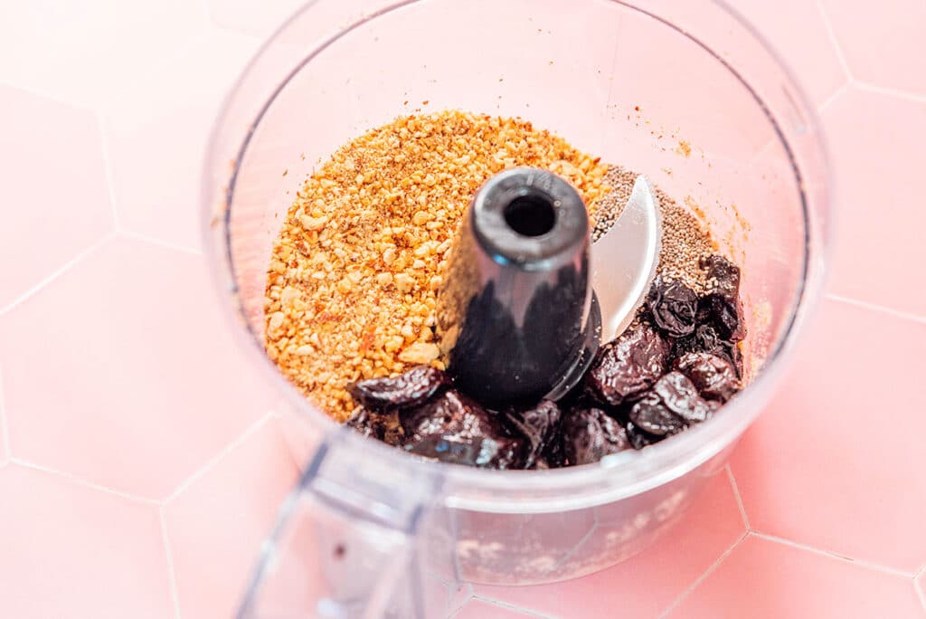 A food processor filled with processed almonds and whole prunes