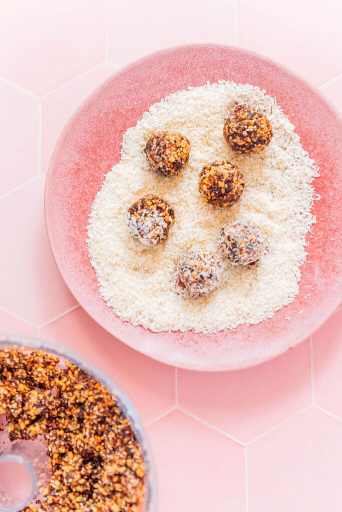 6 coconut coated no bake energy bites sitting on top of layer of shredded coconut inside a pink bowl