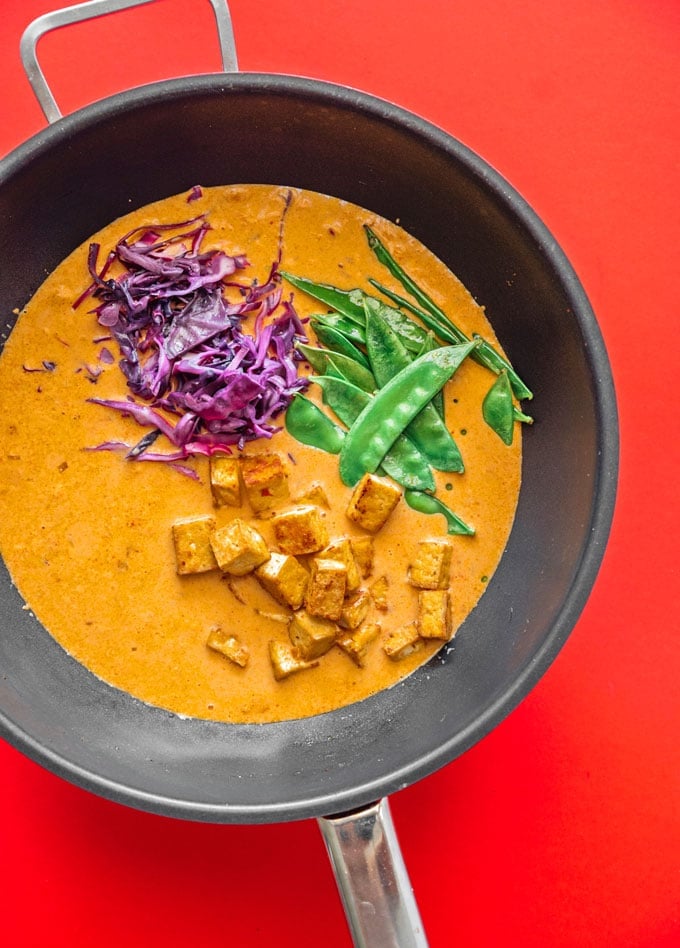 Vegan Thai red curry in a wok on a red background