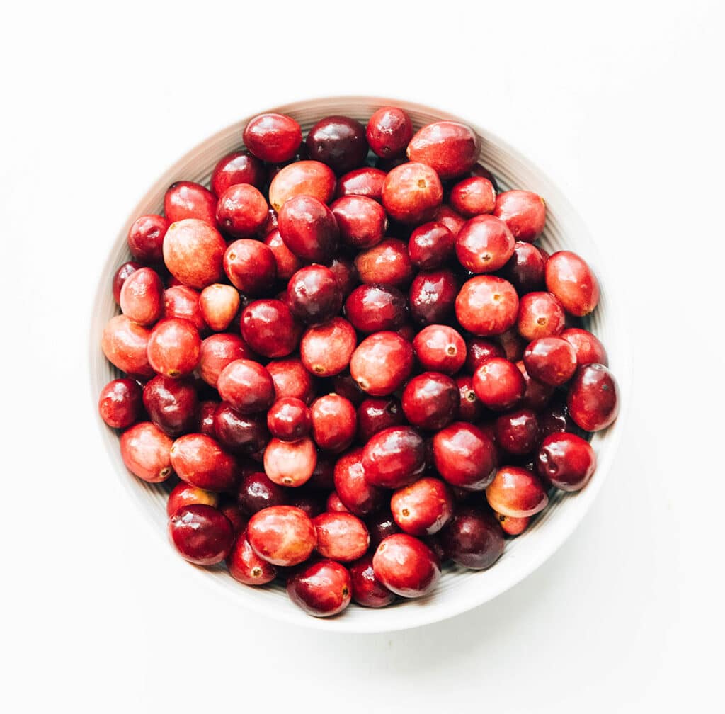 A white bowl filled with cranberries and placed on a white background