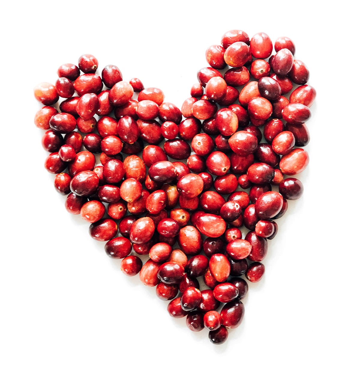 A cup or so of cranberries arranged in a heart shape on a white background