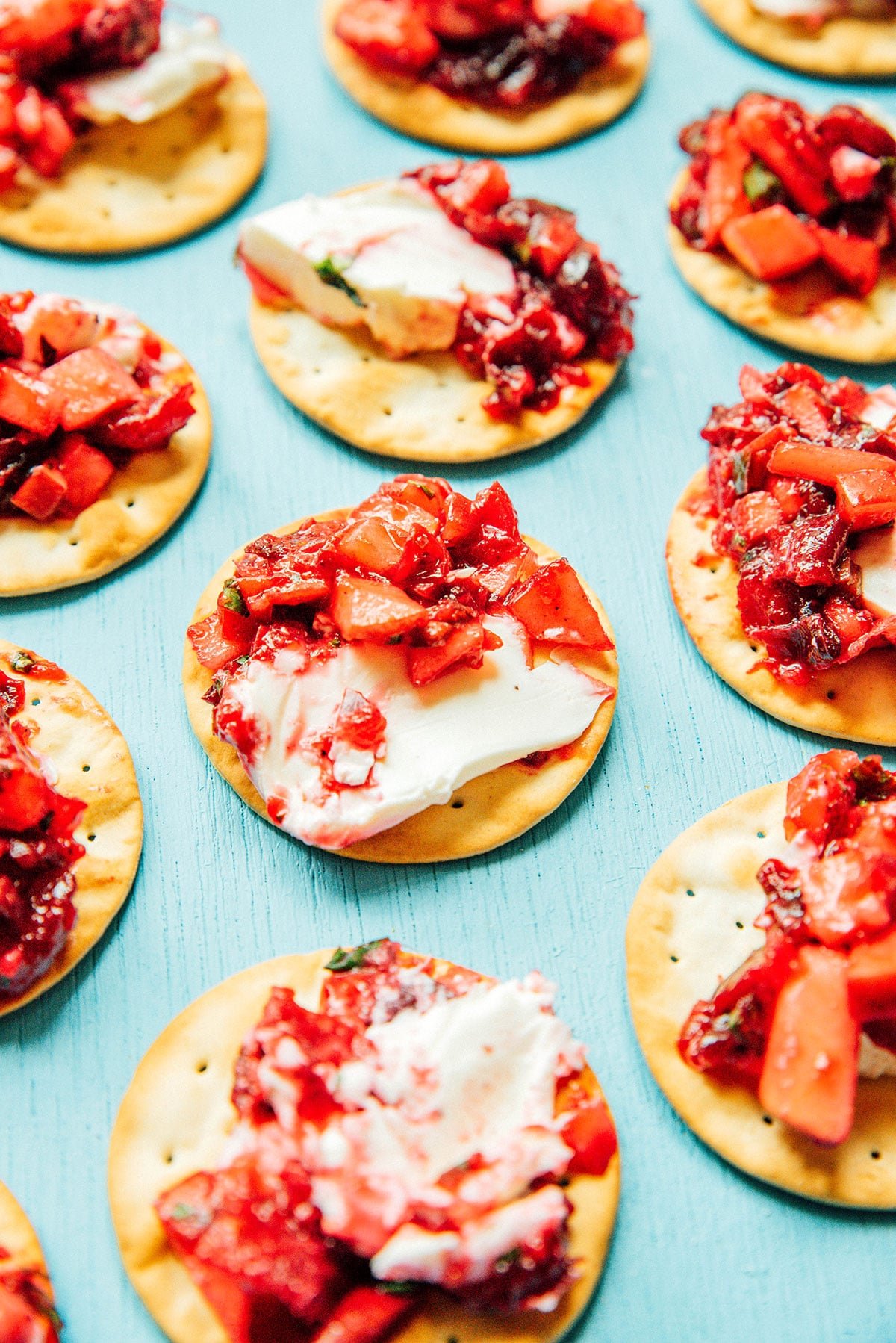 Crackers topped with savory roasted cranberry salsa and neatly arranged in a single layer on a blue background