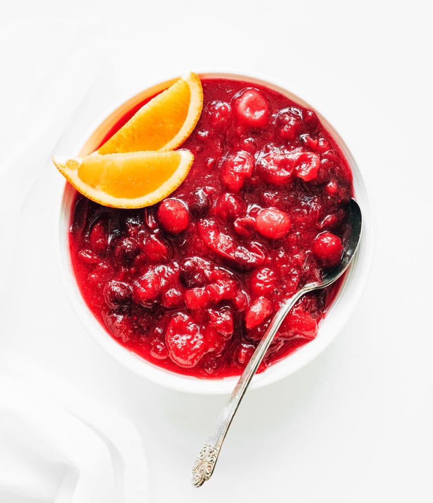 A white bowl filled with homemade cranberry sauce and garnished with two orange slices