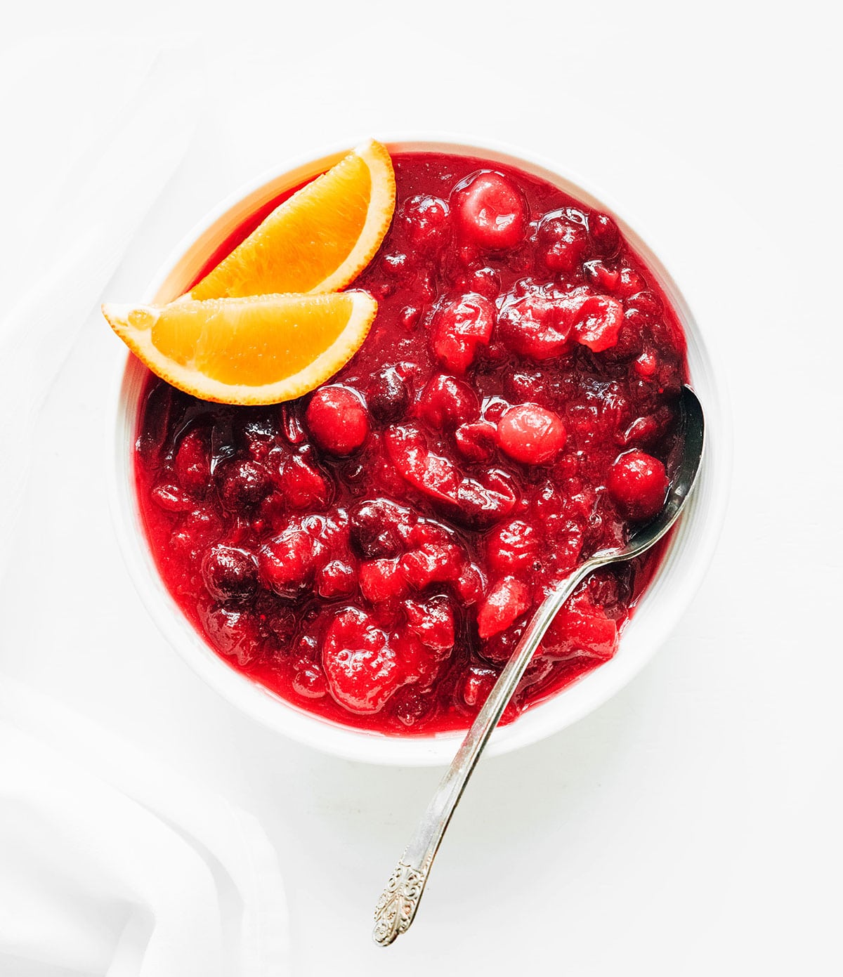 A white bowl filled with homemade cranberry sauce and garnished with two orange slices