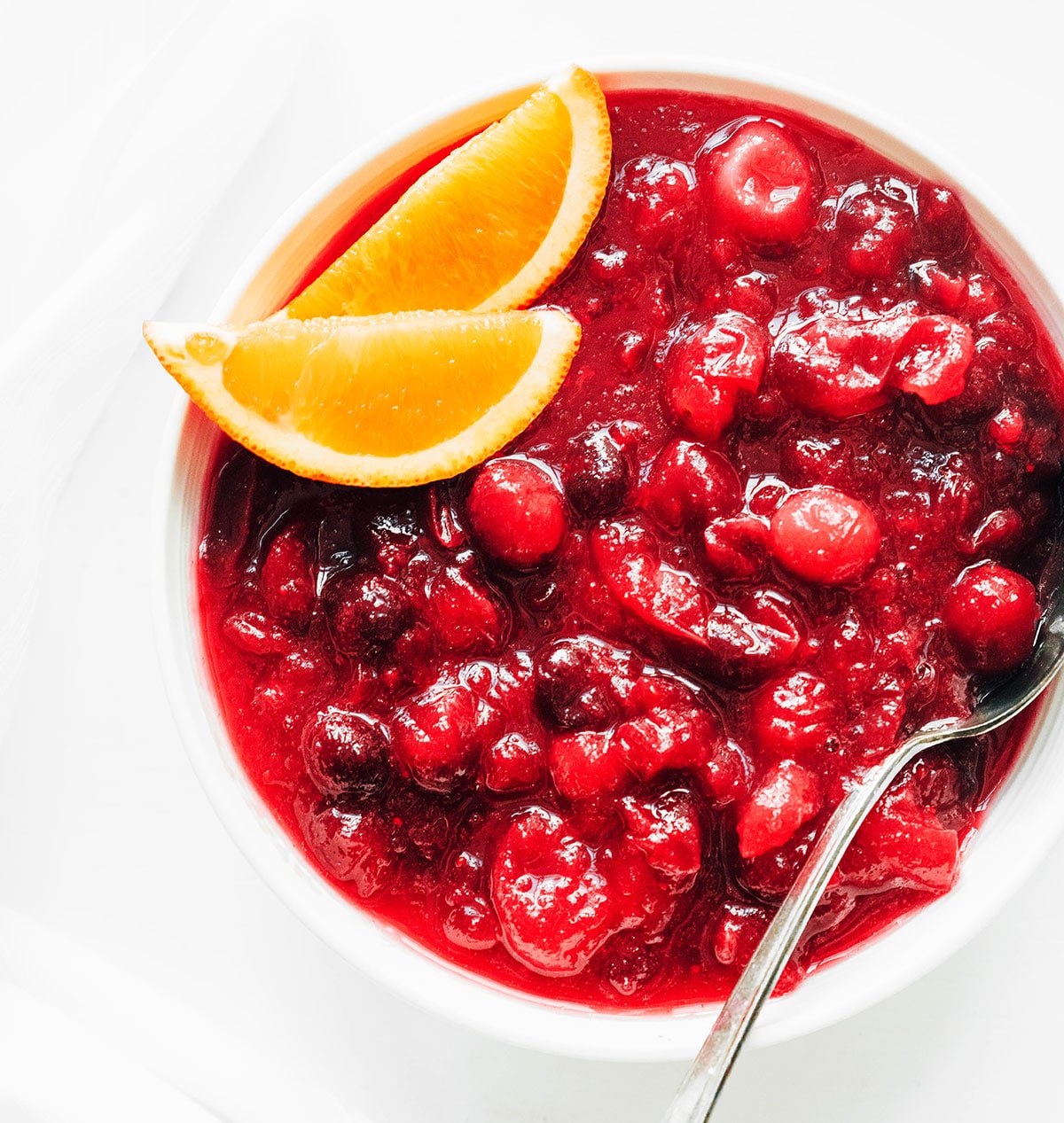 A white bowl filled with cranberry sauce and garnished with orange slices