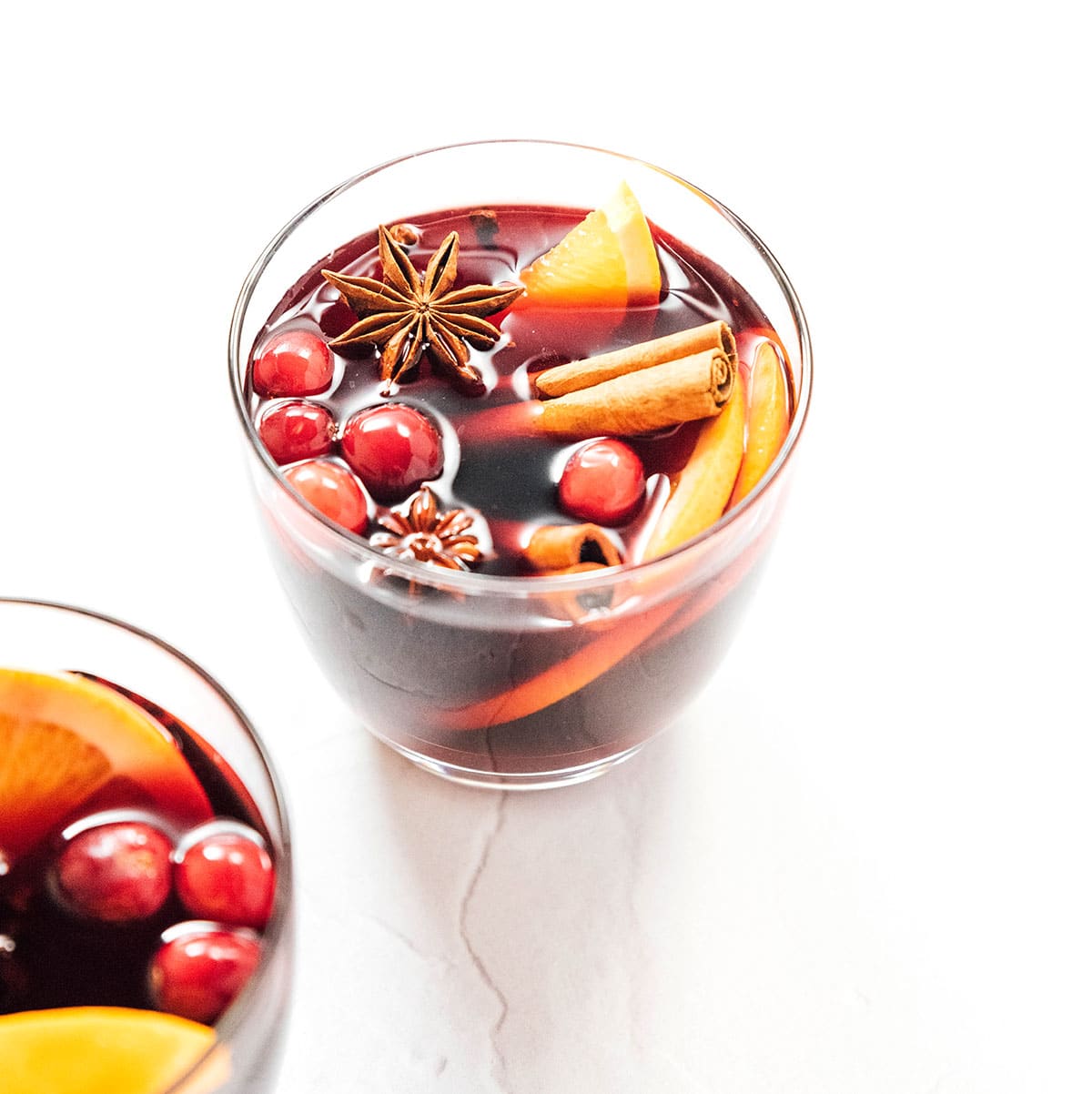 A short glass filled with gluhwein and garnished with orange slices, cinnamon sticks, star anise, and cranberries
