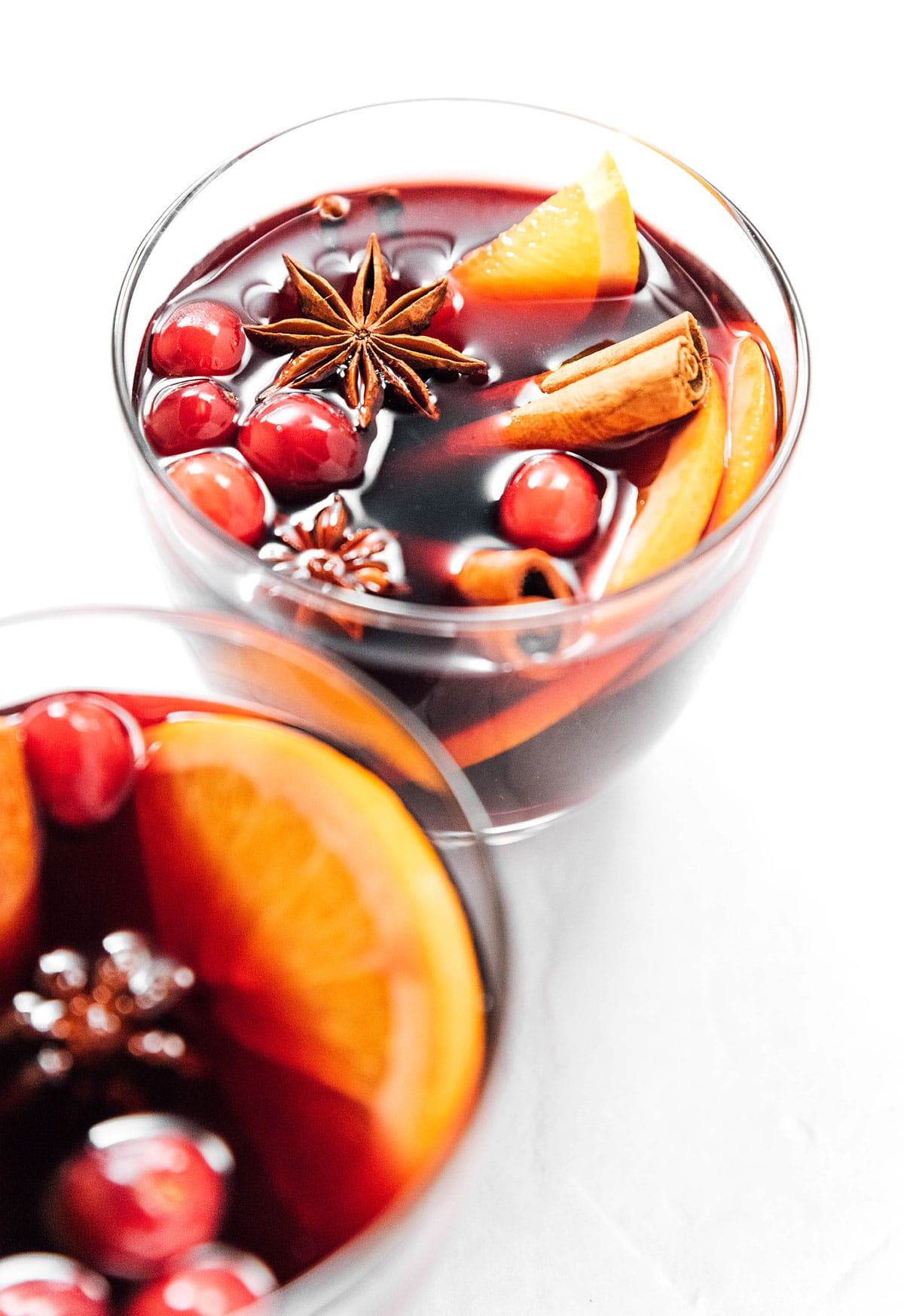 Two short glasses filled with orange mulled wine and garnished with star anise, cranberries, orange slices, and cinnamon sticks