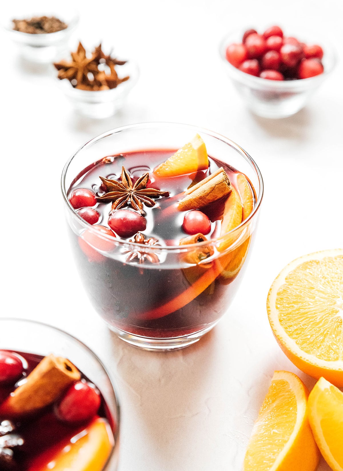 A short glass filled with gluhwein and garnished with orange slices, cinnamon sticks, star anise, and cranberries