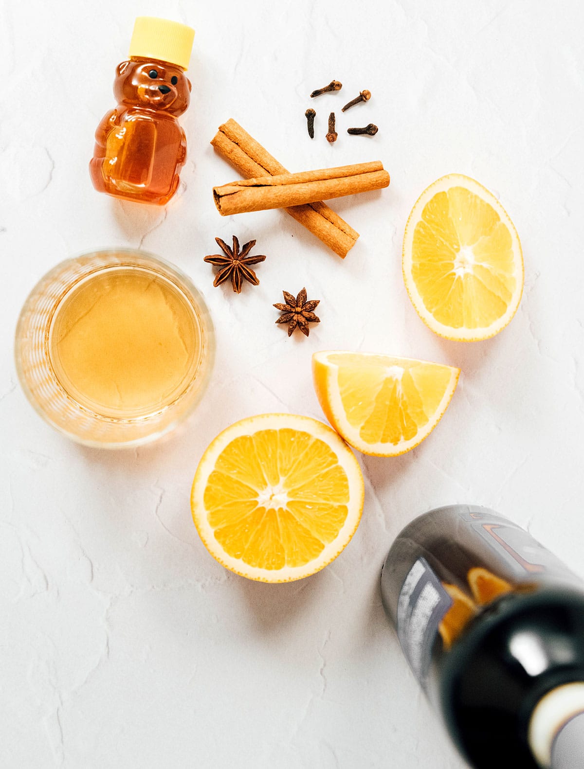 Honey, star anise, cinnamon sticks, a sliced orange, and other gluhwein ingredients arranged on a white background